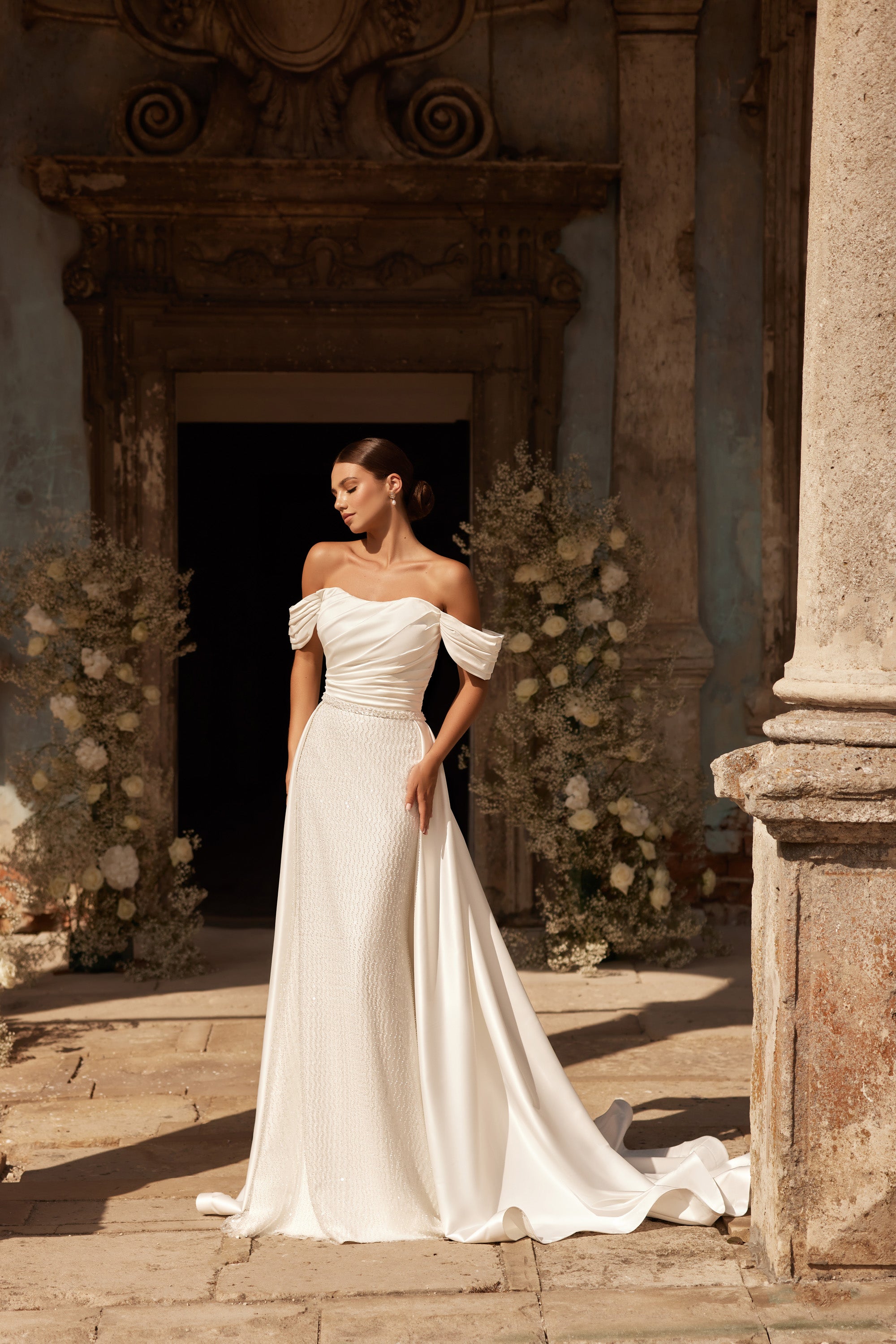 Ivory wedding dress with a fitted beaded skirt, off-the-shoulder sleeves, and a flowing overskirt