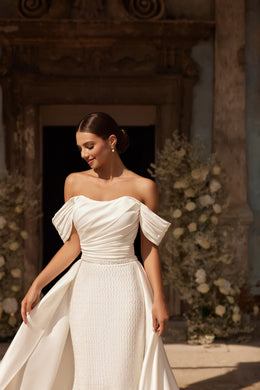 Close-up of an ivory wedding dress with ruched off-the-shoulder bodice and textured embellished skirt