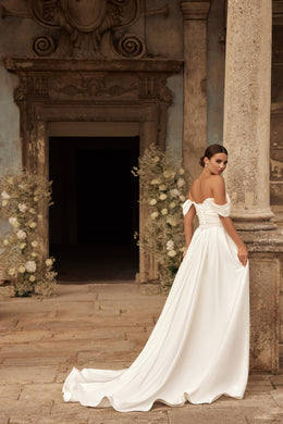 Back view of an ivory wedding dress with off-the-shoulder sleeves, flowing overskirt, and sweeping train