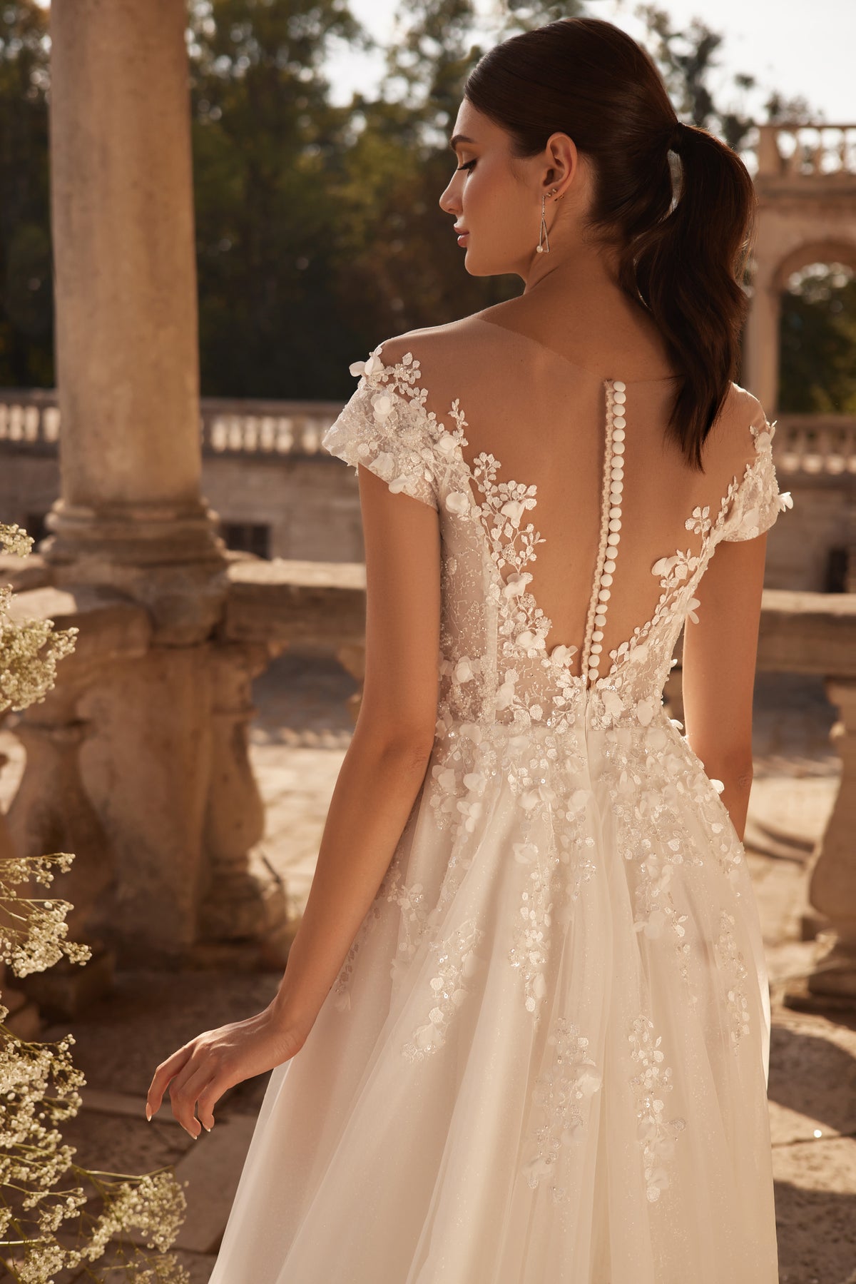 Illusion lace back on an ivory wedding dress, finished with pearl-like buttons, cap sleeves, and floral appliqués