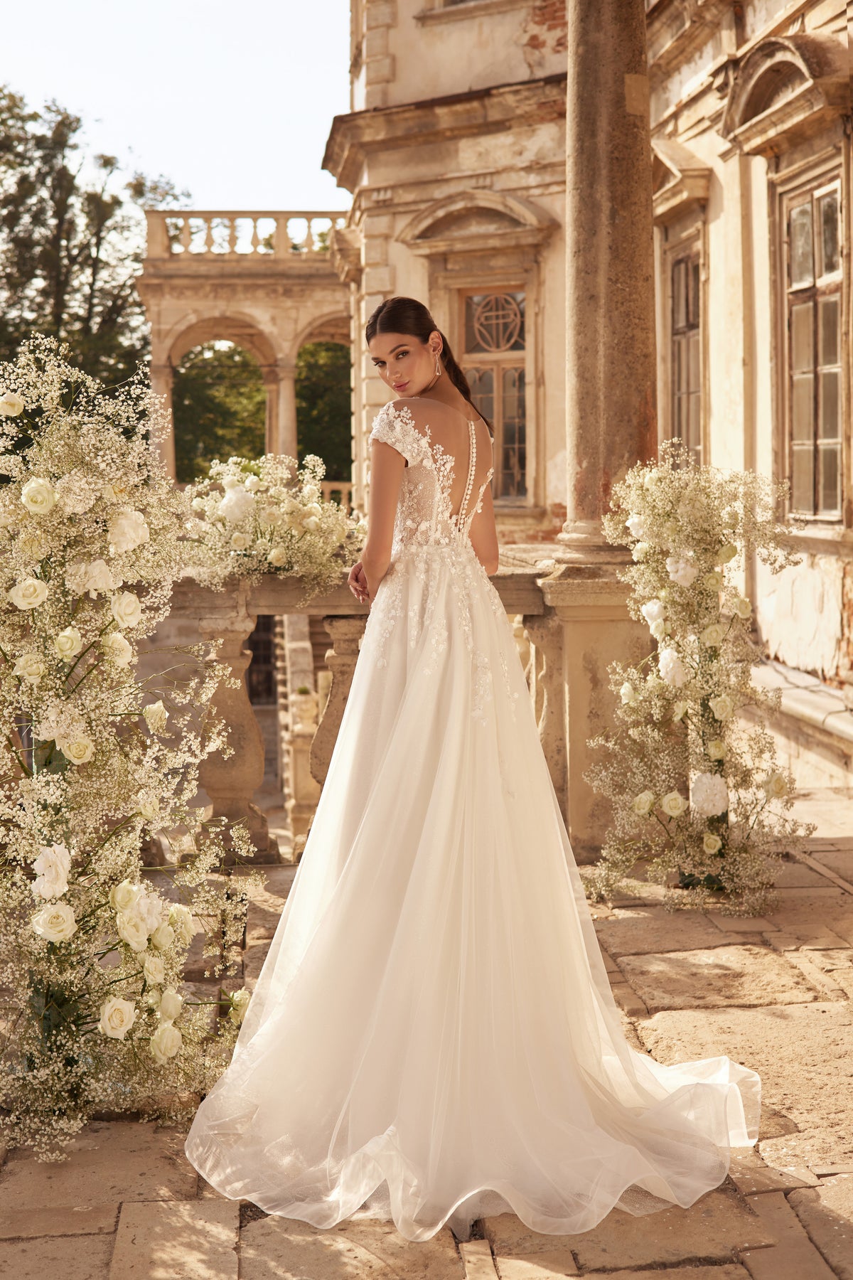 Flowing ivory wedding dress with a long train, floral lace back, and sheer cap sleeves