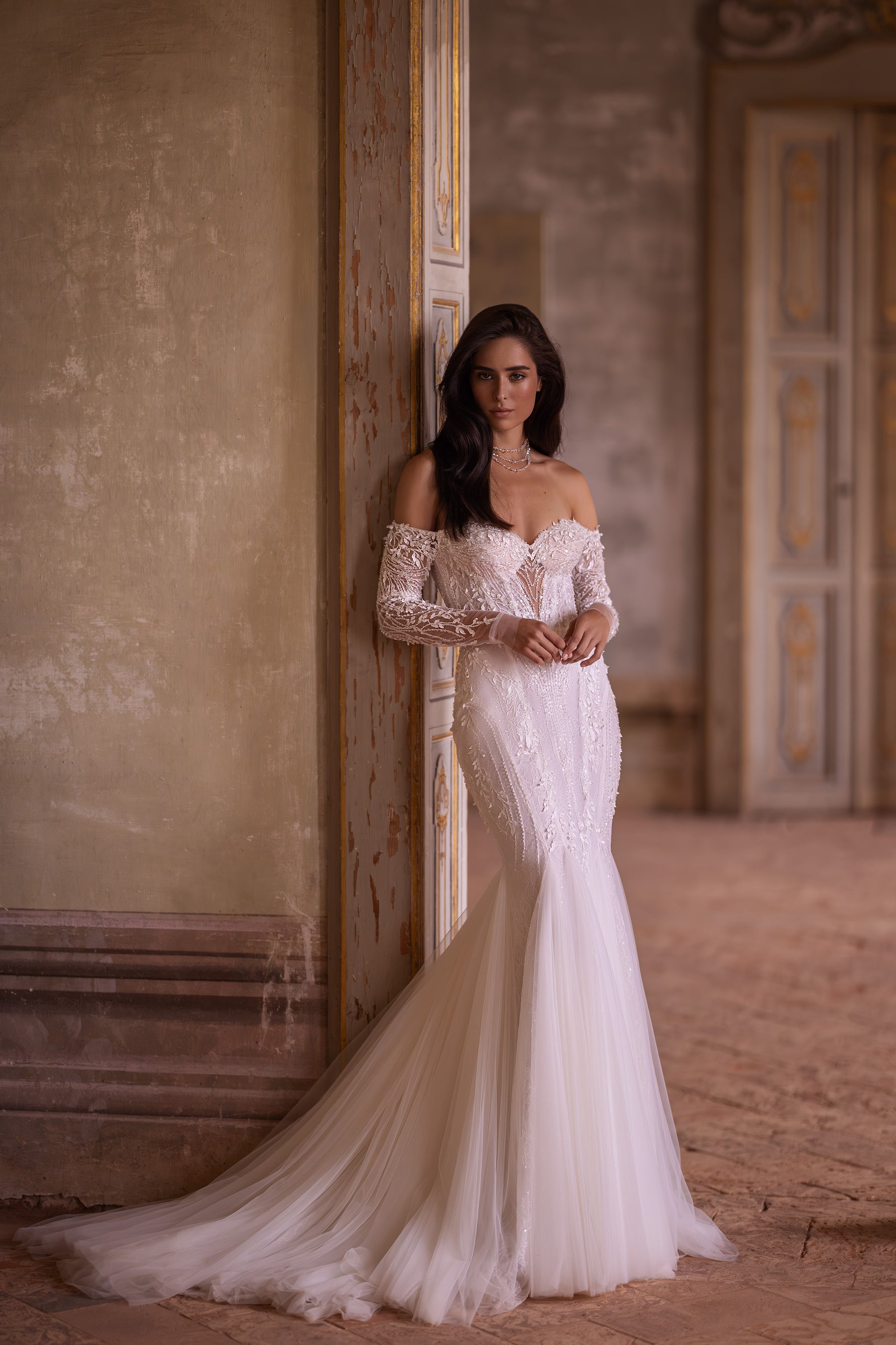 Ivory mermaid wedding dress with long lace sleeves, off-the-shoulder neckline, and an extended train