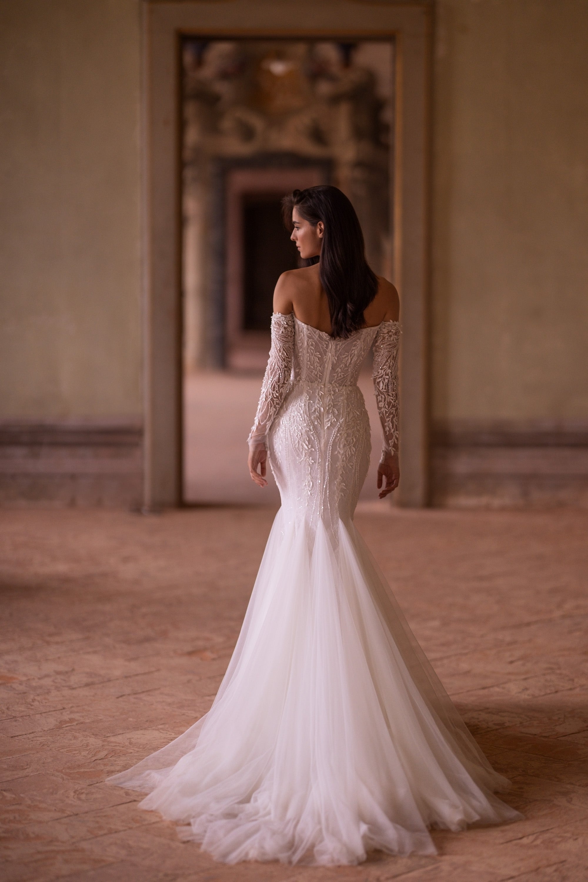 Ivory mermaid wedding dress showing a lace-covered back, off-the-shoulder sleeves, and a long flowing train
