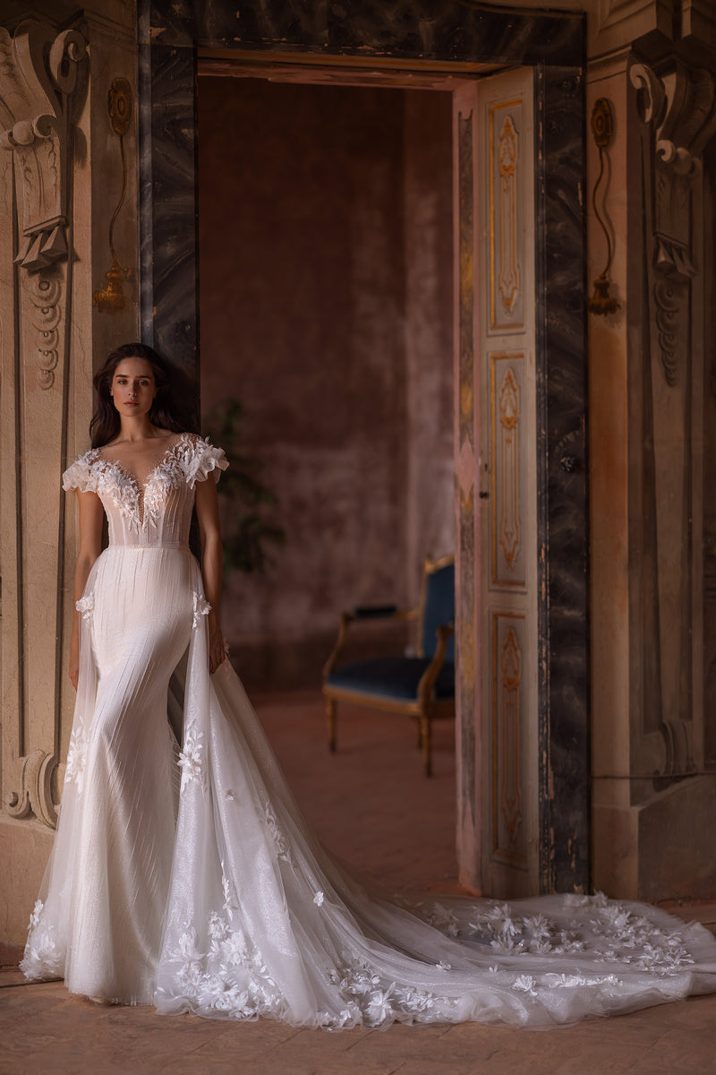 Ivory mermaid wedding dress with floral lace, ruffled sleeves, fitted bodice, and a flowing overskirt