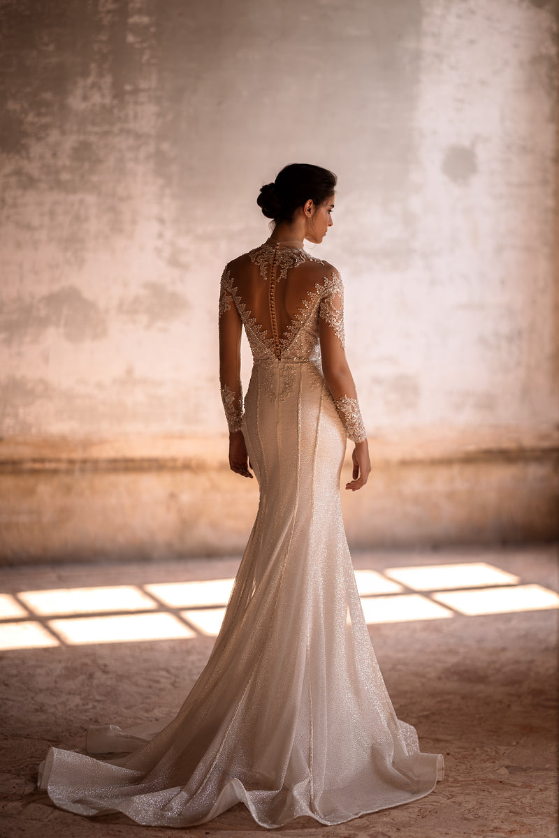 Beaded open-back wedding dress with sheer long sleeves, a fitted silhouette, and a pooled train