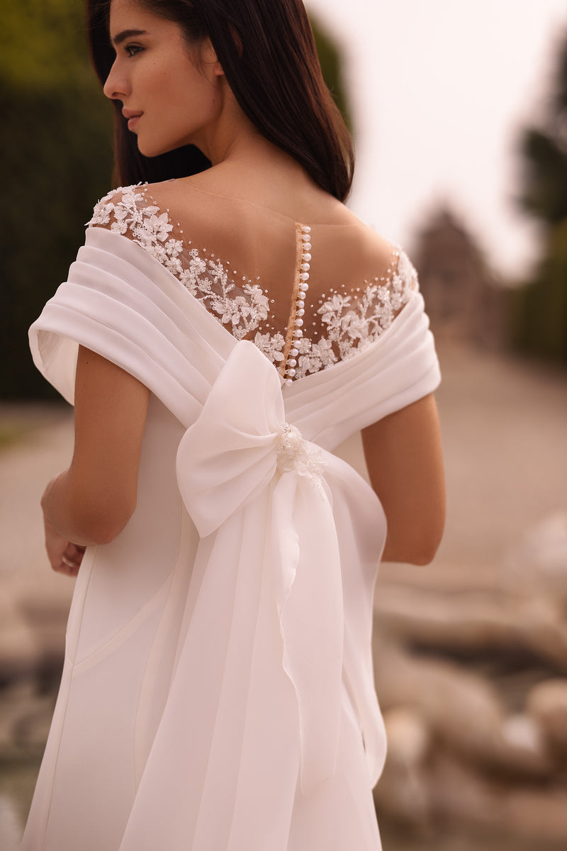 Sheer lace back with pearl-like buttons, an oversized bow, and flowing train on an ivory wedding dress