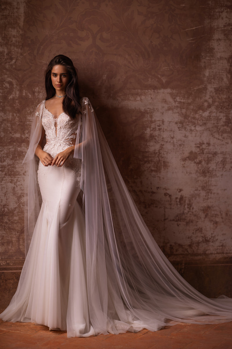 Ivory trumpet wedding dress with a deep V-neck, beaded lace bodice, sheer tulle drapes, and a long train