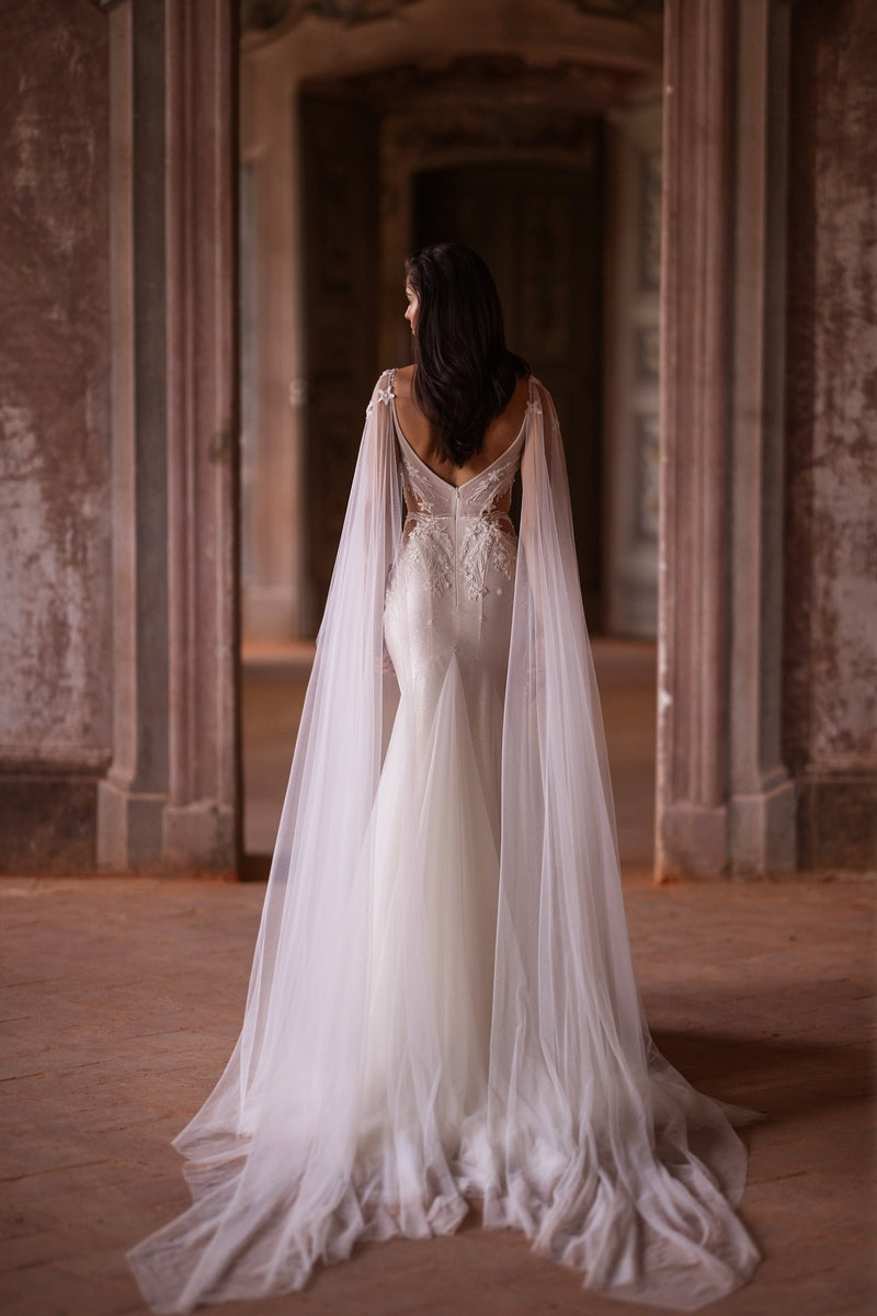 Deep V open back with lace detailing and flowing sheer tulle drapes on an ivory trumpet wedding dress