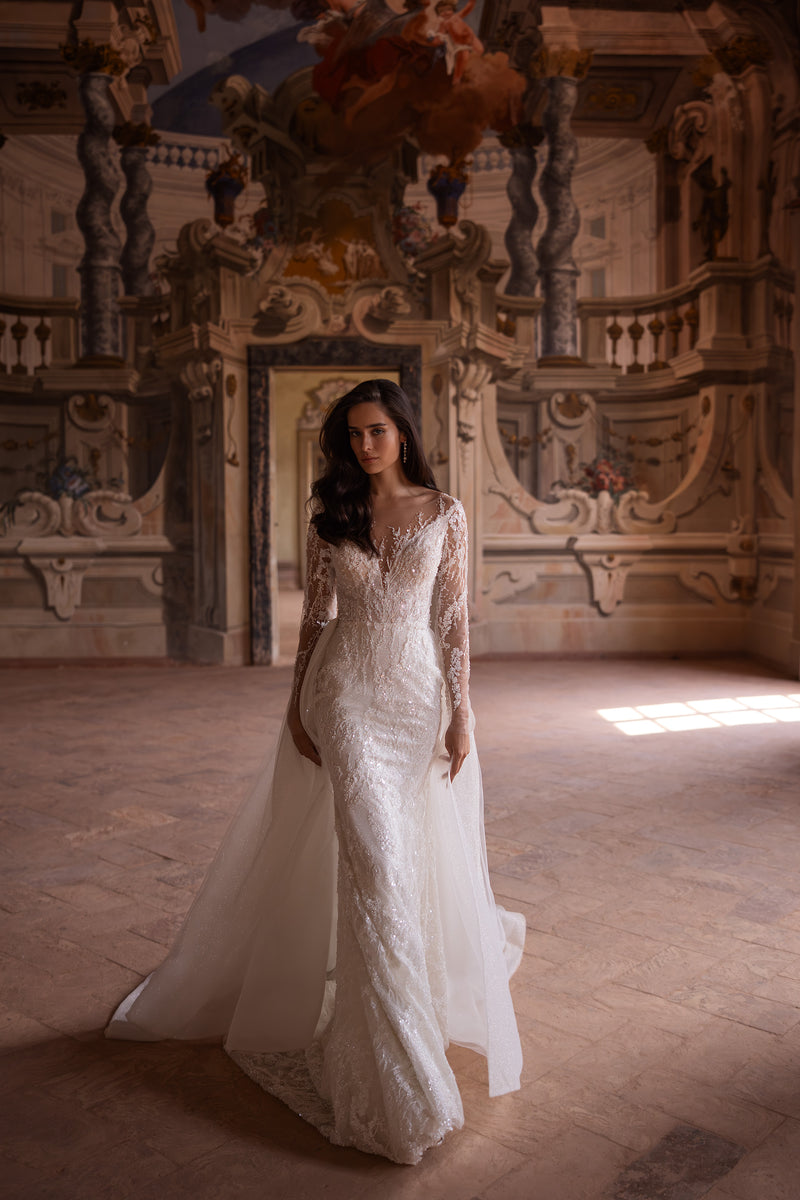 Ivory trumpet wedding dress with long sheer lace sleeves, V-neckline, and a sweeping overskirt train