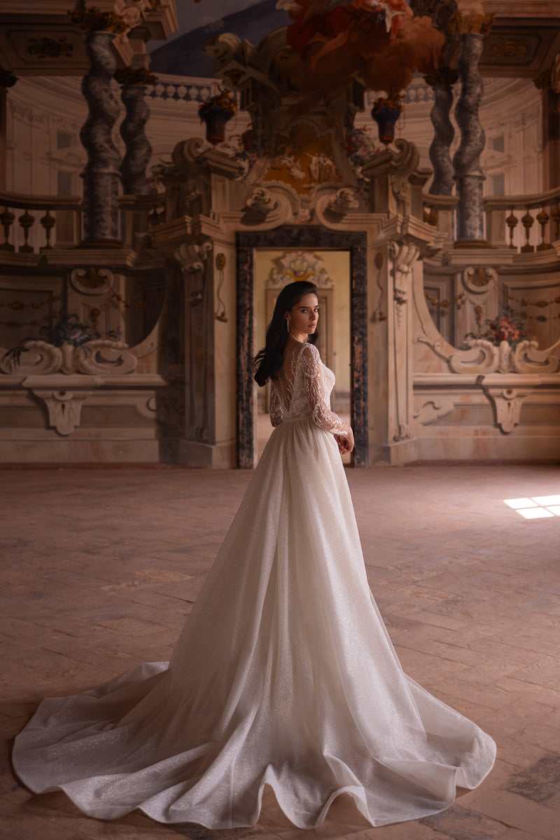 Ivory wedding dress with long lace sleeves, a layered full overskirt, and a glittering floor-length train