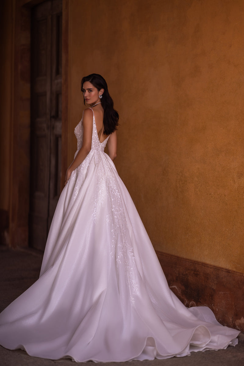 Open-back ivory wedding dress with thin straps, a full glittering skirt, and long train