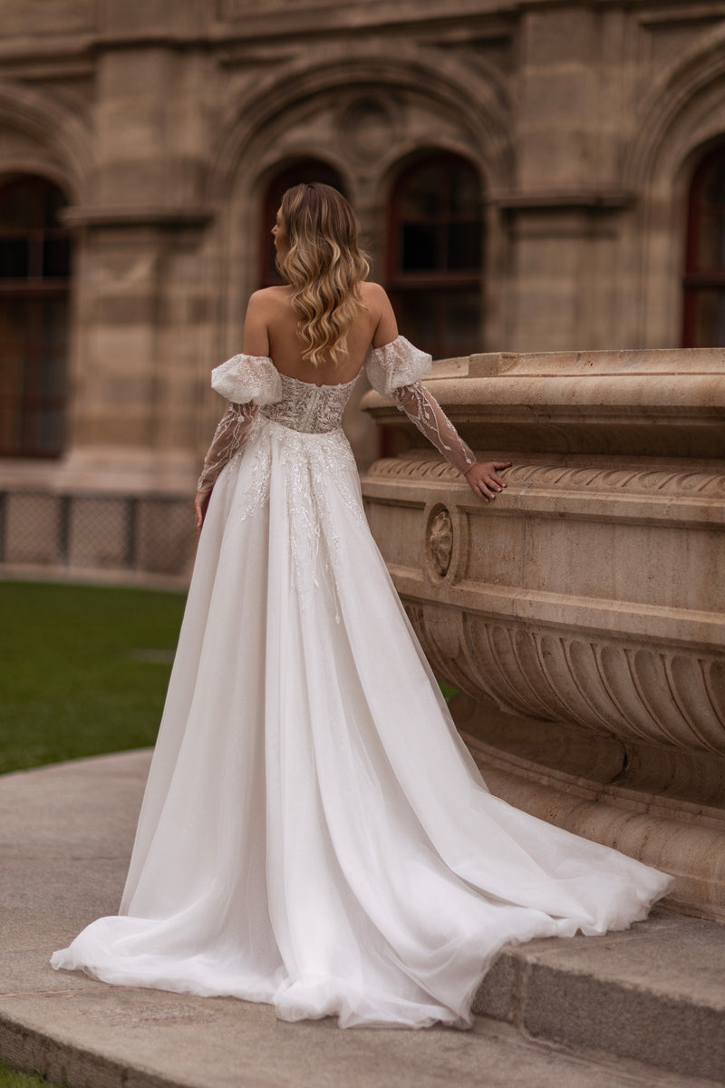 Open-back ivory wedding dress with beaded lace details, sheer off-shoulder sleeves, and a sweeping train