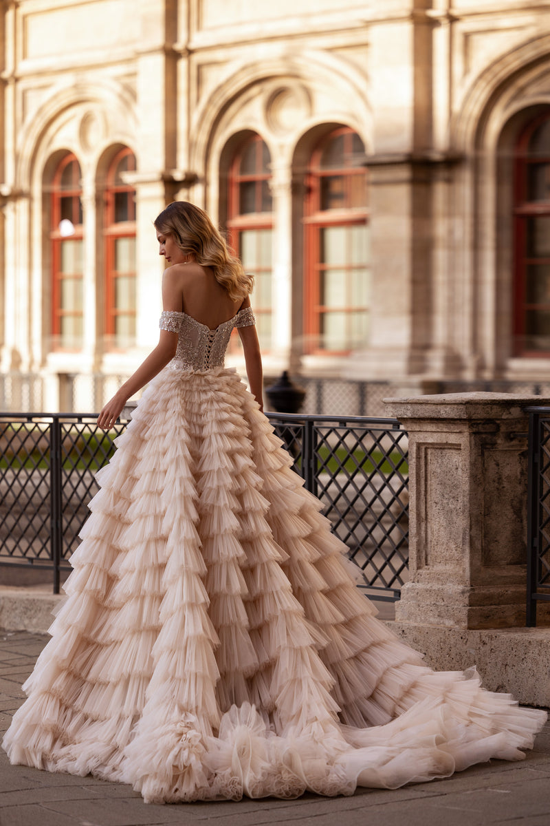 Open back on an ivory wedding dress with an off-shoulder crystal bodice and long ruffled train