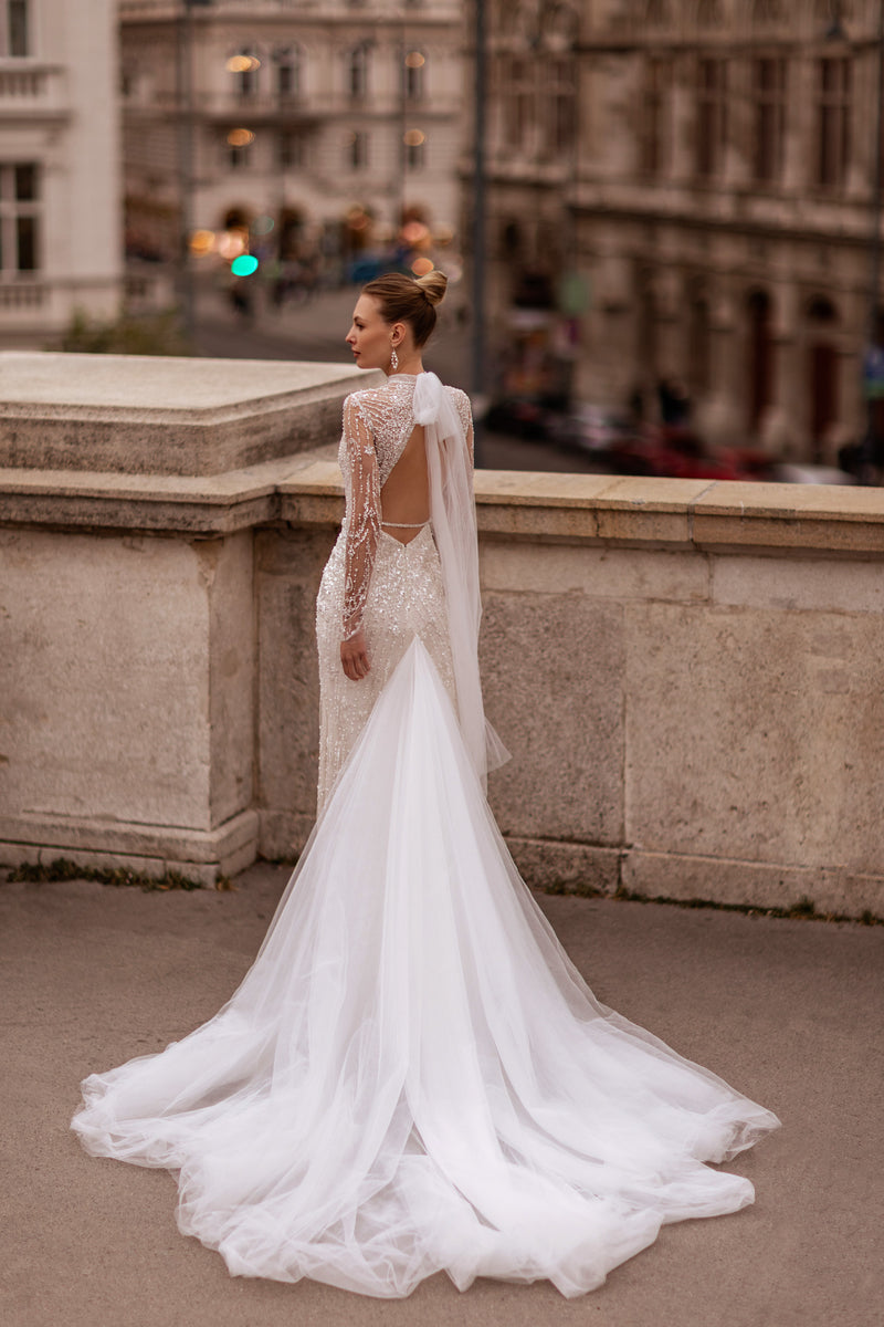 Open-back wedding dress with beaded sheer sleeves, a fitted silhouette, and a dramatic floor-length train