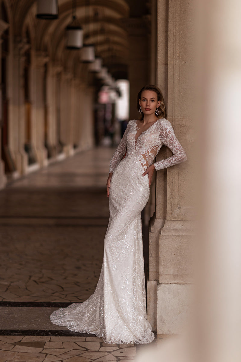 Ivory mermaid wedding dress with sheer long sleeves, plunging V-neckline, lace embellishments, and sweeping train