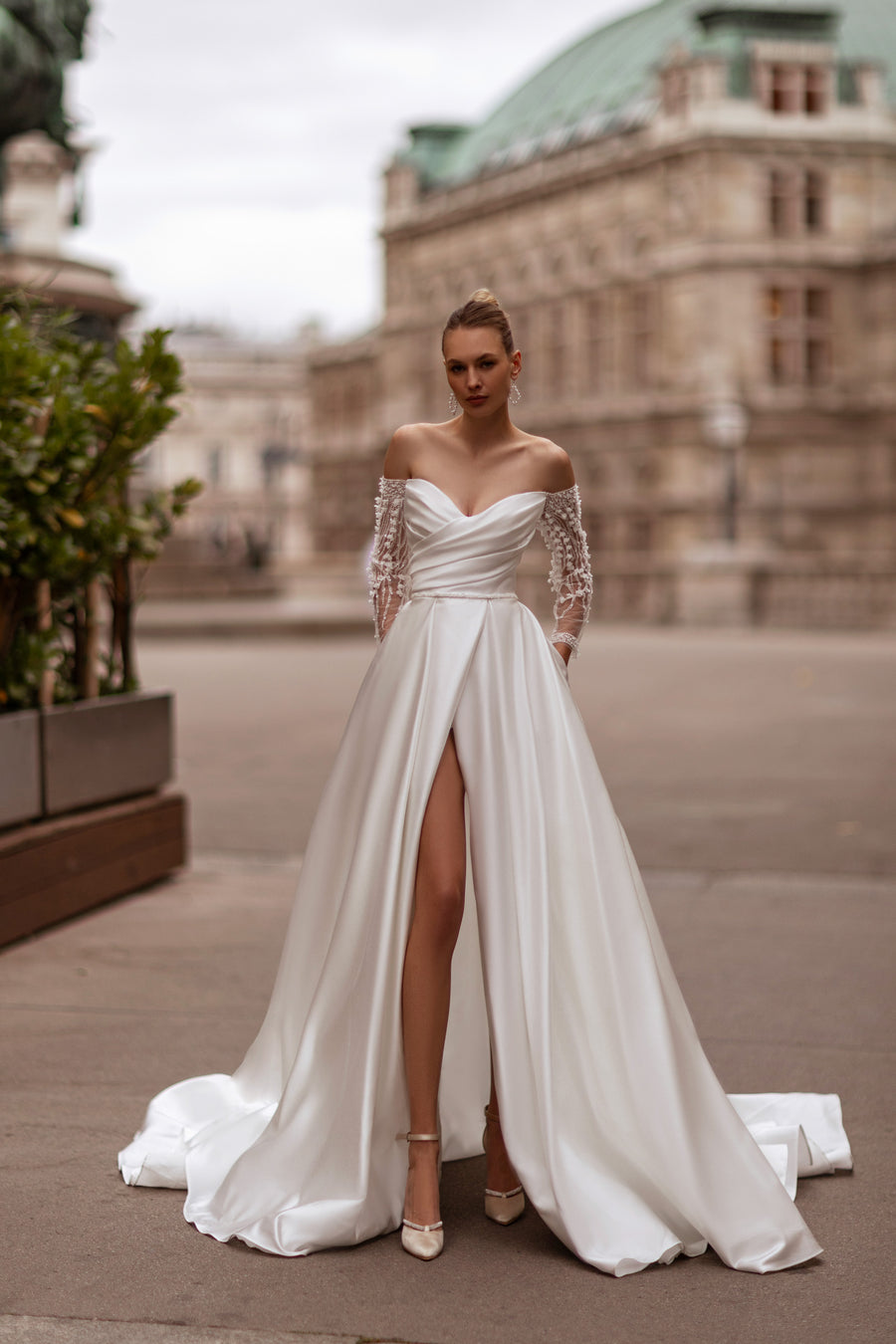Ivory A-line wedding dress with a draped neckline, lace sleeves, high slit, and sweeping train