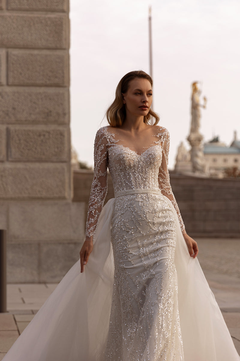 Ivory beaded wedding dress with long sheer sleeves, an illusion neckline, fitted skirt, and flowing train