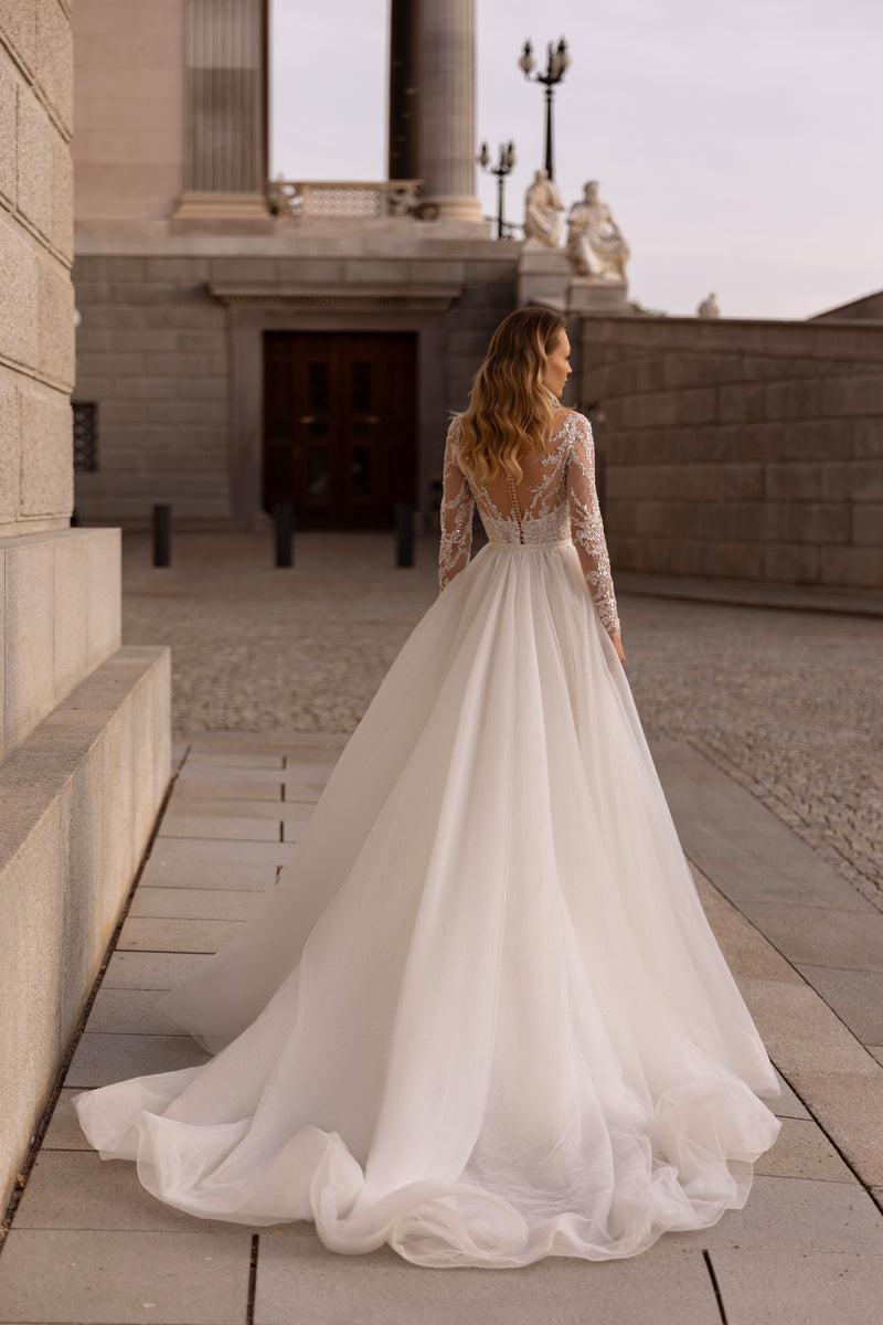 Ivory wedding dress with a sheer beaded back, long sleeves, and a full tulle train spreading behind