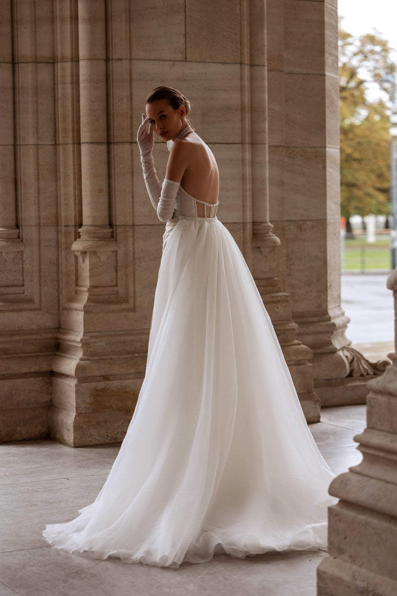 Open-back ivory wedding dress with a full flowing skirt, glittering bodice, and long cathedral train