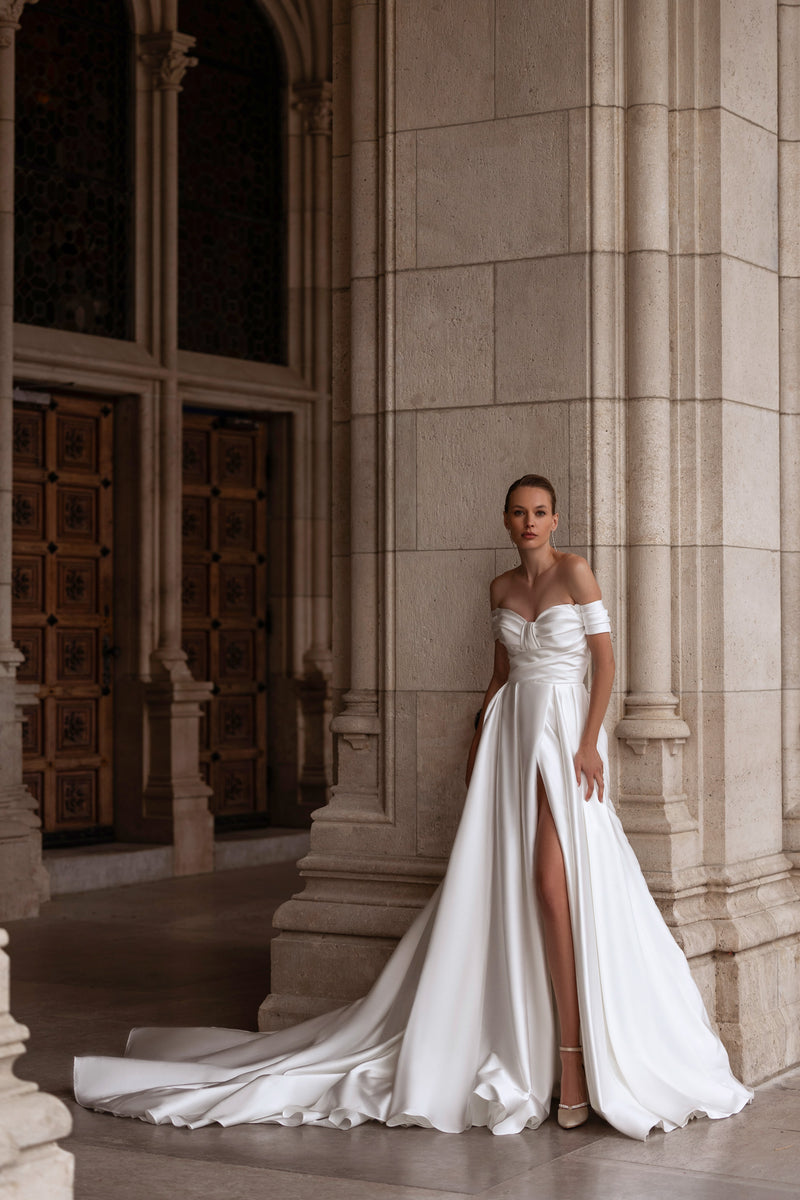 Ivory A-line wedding dress with an off-the-shoulder draped bodice, thigh-high slit, and long train