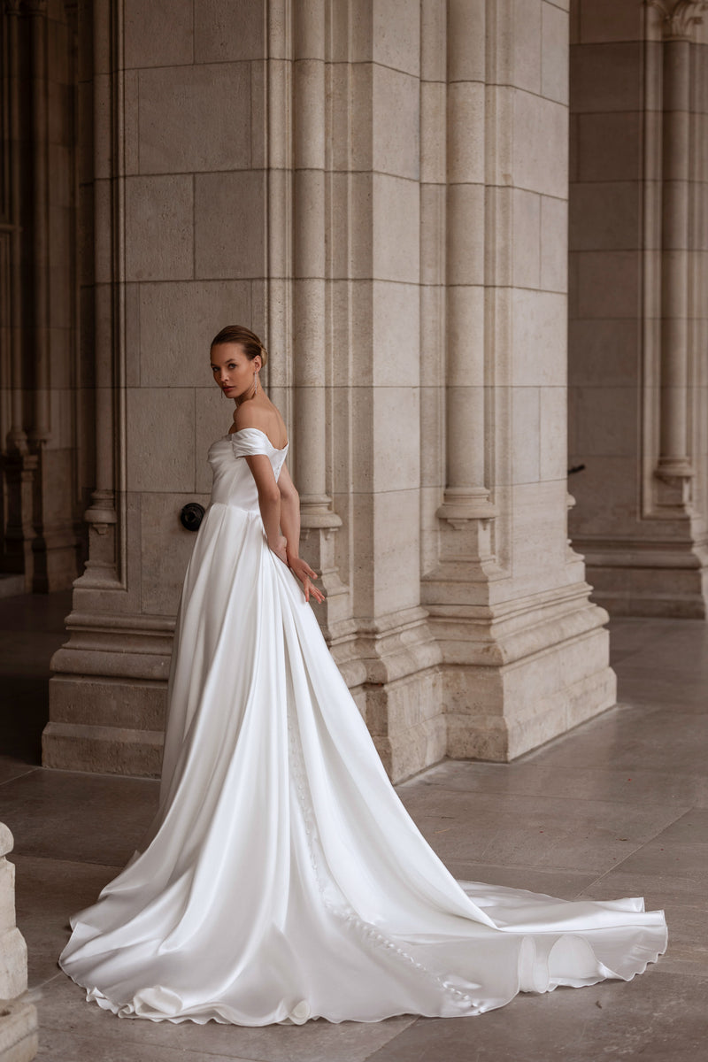 Flowing ivory wedding dress with off-the-shoulder sleeves, a sweeping A-line skirt, and extended train
