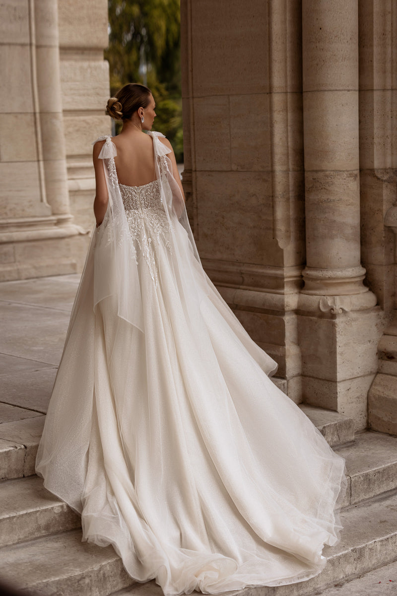 Open-back wedding dress with sheer lace straps, a full skirt, floral appliqués, and a sweeping train