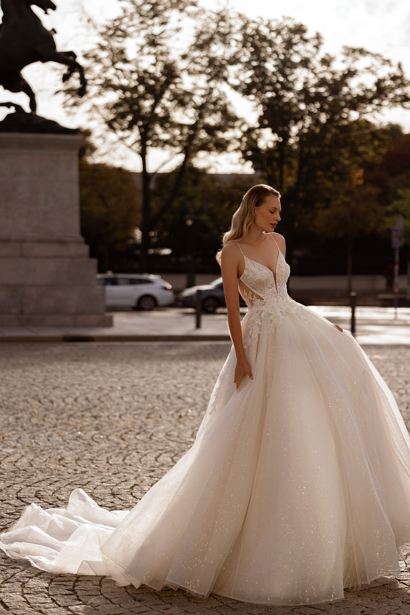 Ivory ball gown wedding dress with a lace bodice, thin straps, sparkling full skirt, and sweeping train