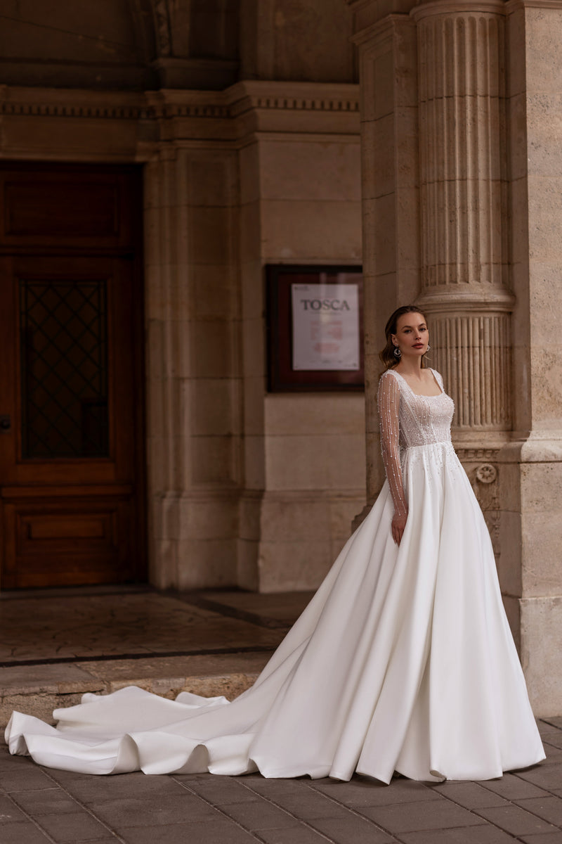 Ivory ball gown wedding dress with a square neckline, sheer beaded sleeves, and a sweeping train