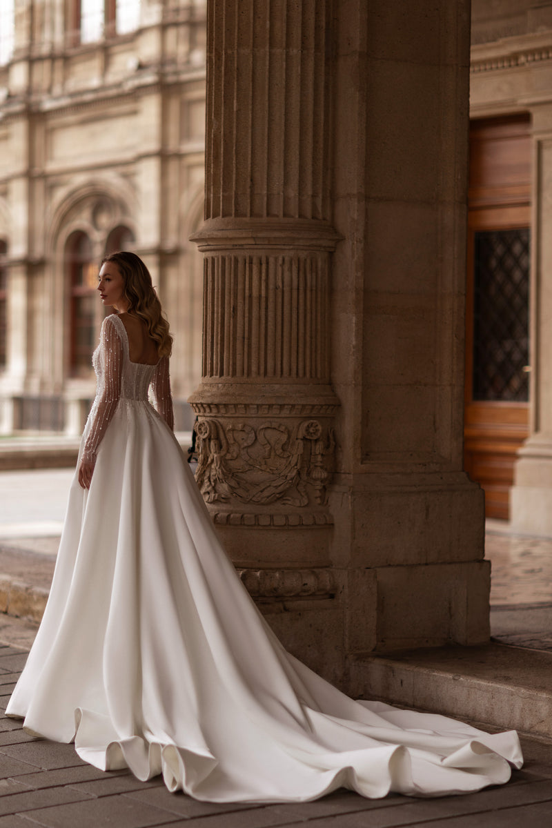 Ivory wedding dress with a full ball gown skirt, sheer beaded sleeves, and a long flowing train