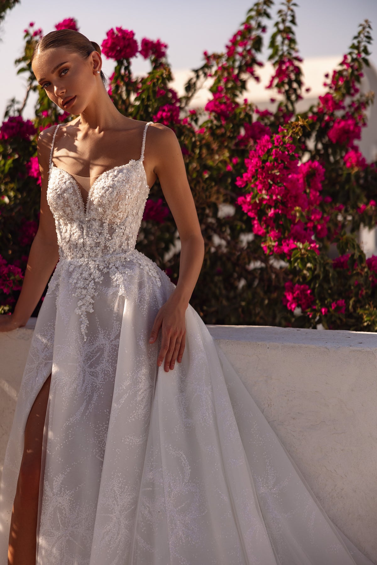 Sparkling floral appliqués cover the bodice of an ivory wedding dress with a V-neckline and front slit