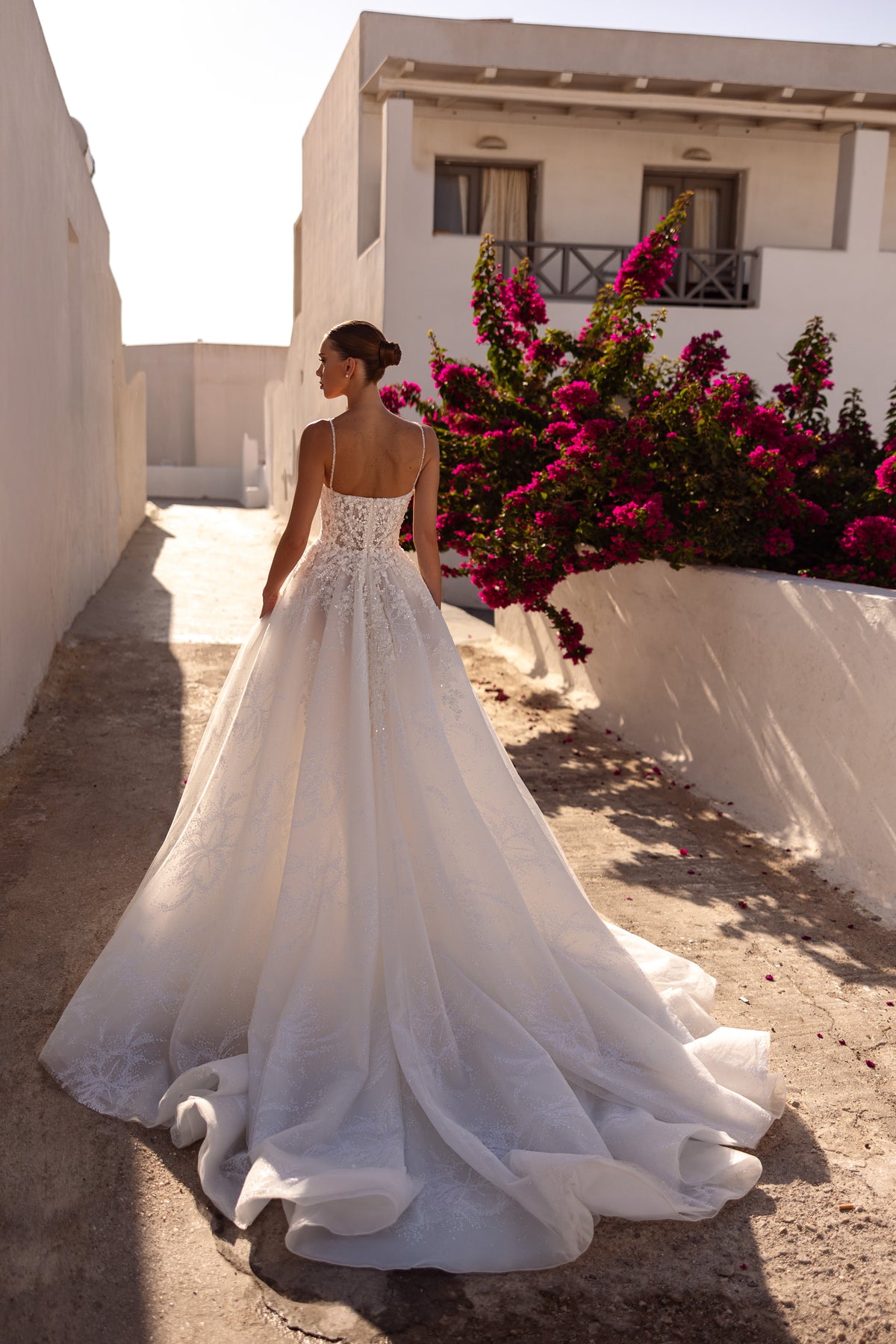 Back of an ivory wedding dress showing a low square back, thin straps, floral detailing, and a long train