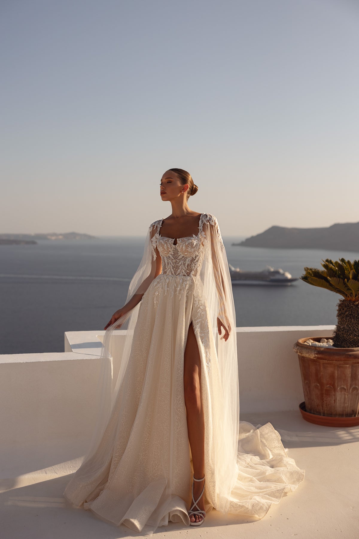 Ivory wedding dress with a square neckline, sheer embellished sleeves, beaded bodice, and thigh-high slit
