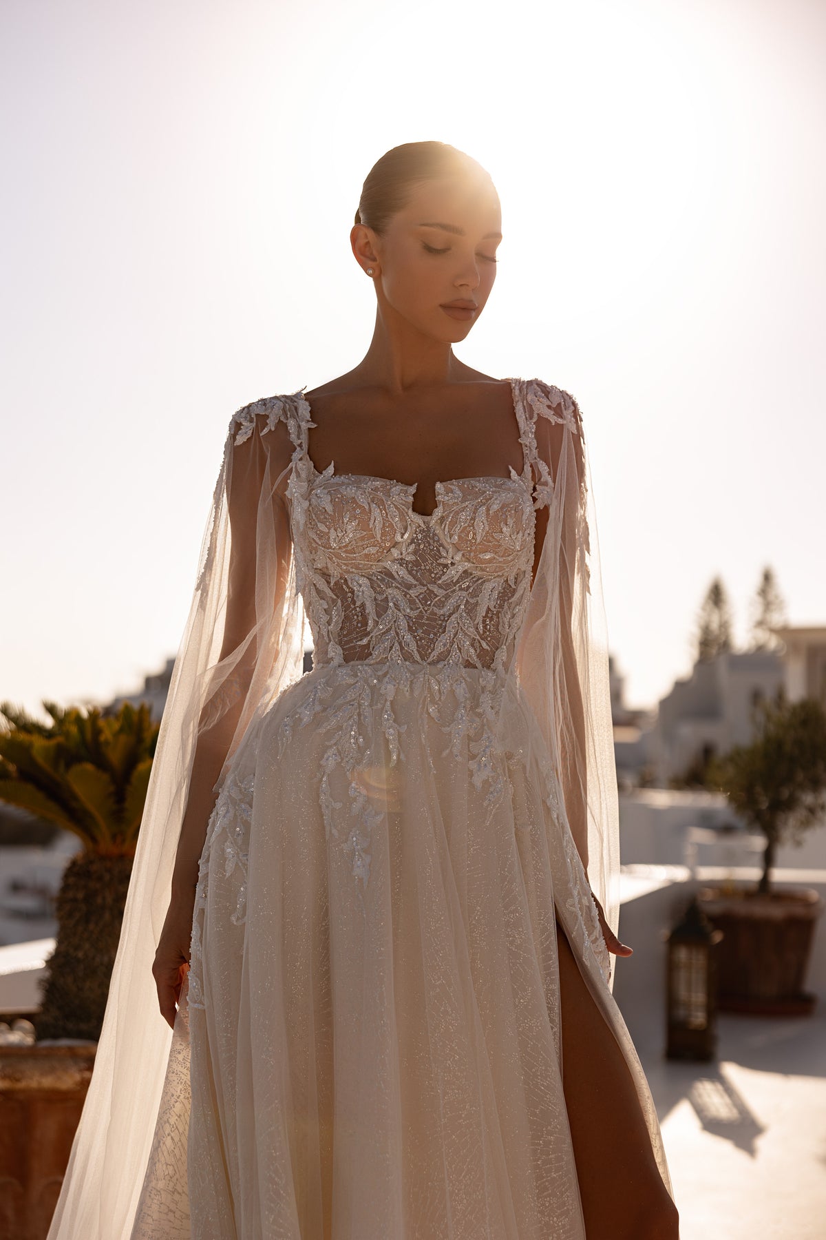 Ivory wedding dress featuring a square neckline, ornate beaded lace bodice, sheer long sleeves, and a front slit