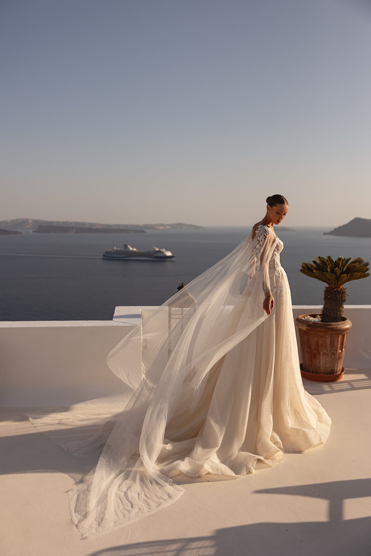 Flowing sheer cape and extended train trail behind this ivory wedding dress in a side view
