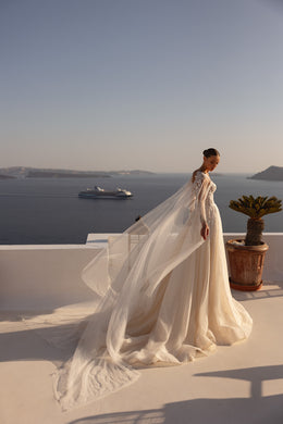 Flowing sheer cape and extended train trail behind this ivory wedding dress in a side view