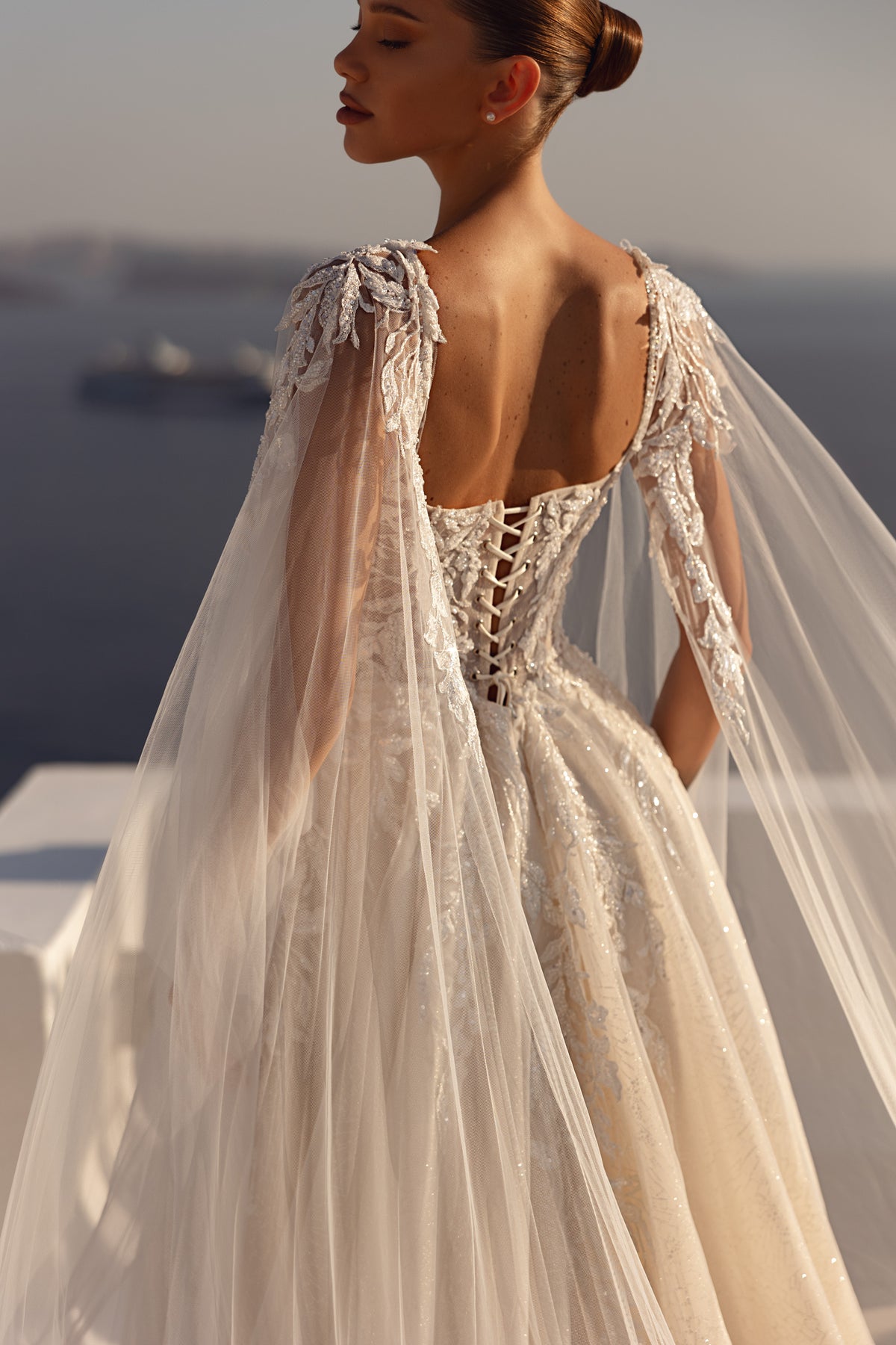 Open lace-up back and sheer embellished cape on an ivory wedding dress