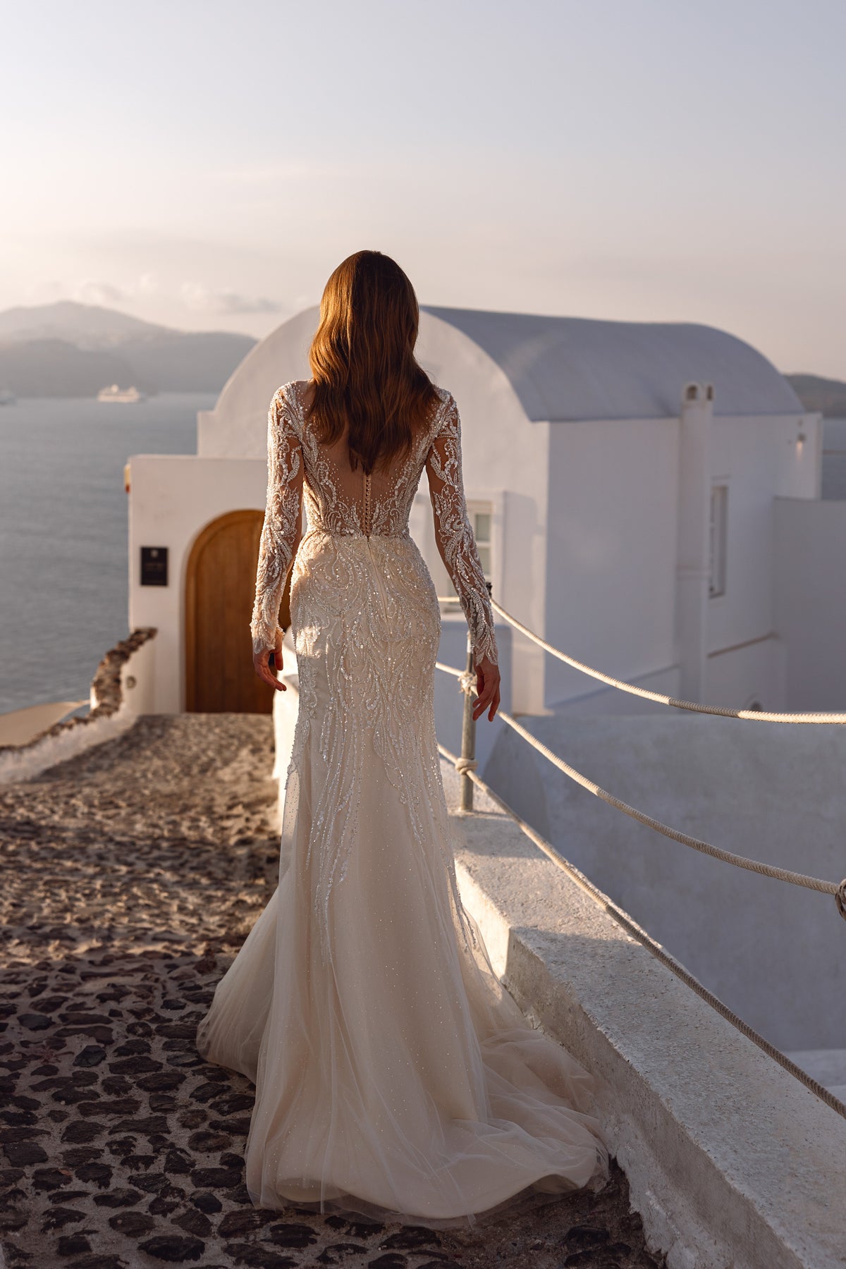 Ivory wedding dress with a low V-shaped sheer back, long beaded sleeves, and a slim skirt extending into a train