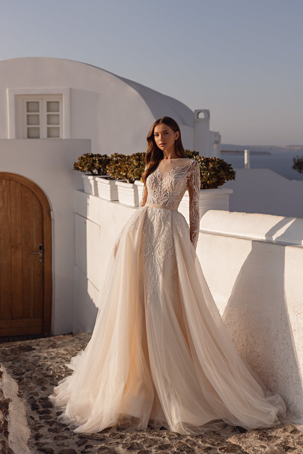 Long-sleeve ivory wedding dress with shimmering floral embellishments, a defined waist, and a flowing full skirt