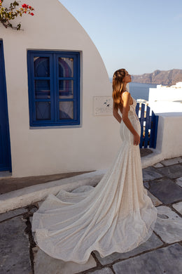 Ivory wedding dress shown from the back with a fitted mermaid silhouette, thin straps, and a long beaded train