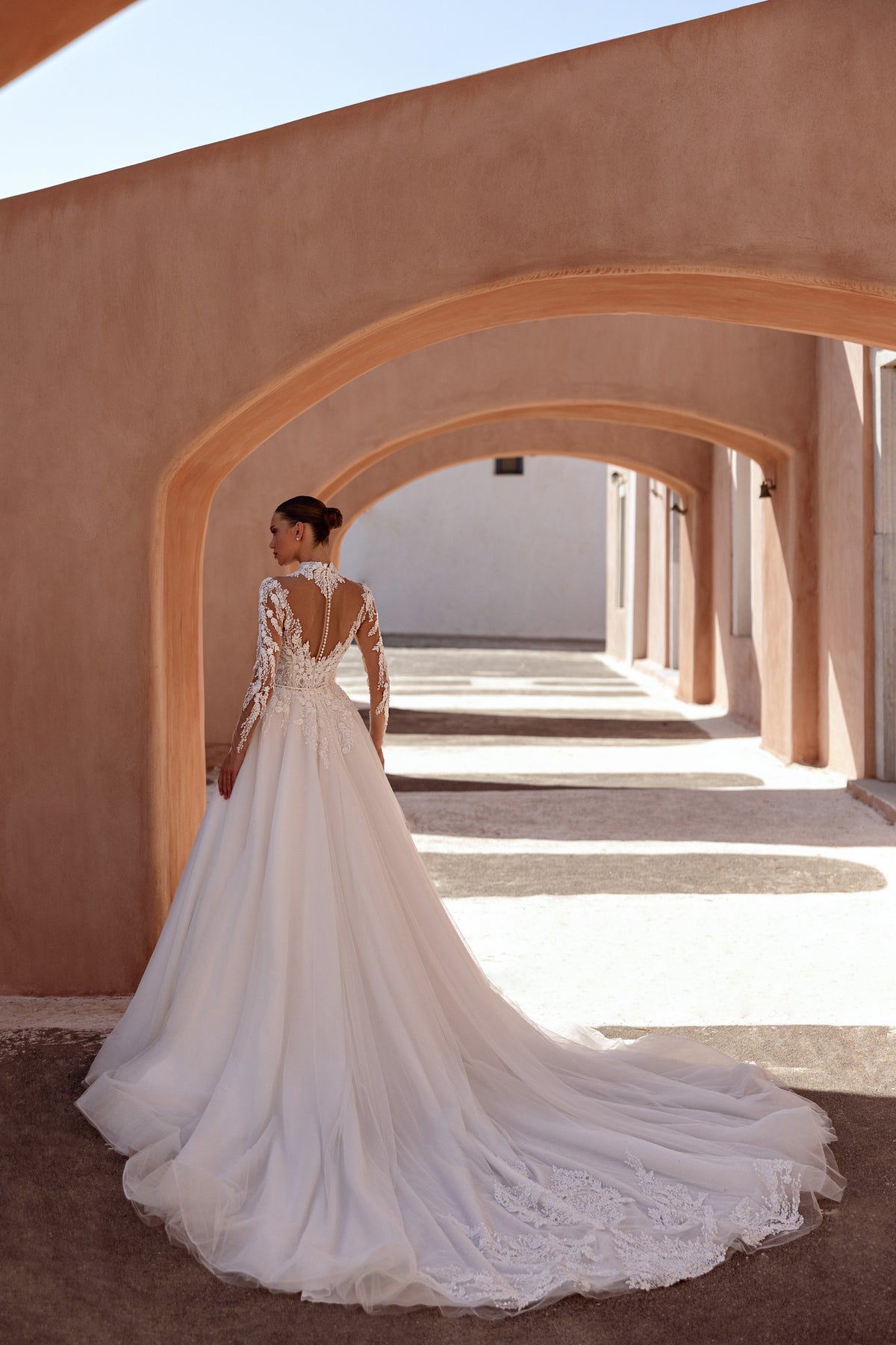 Ivory wedding dress showing a sheer lace back, button closure, long sleeves, and an extended train