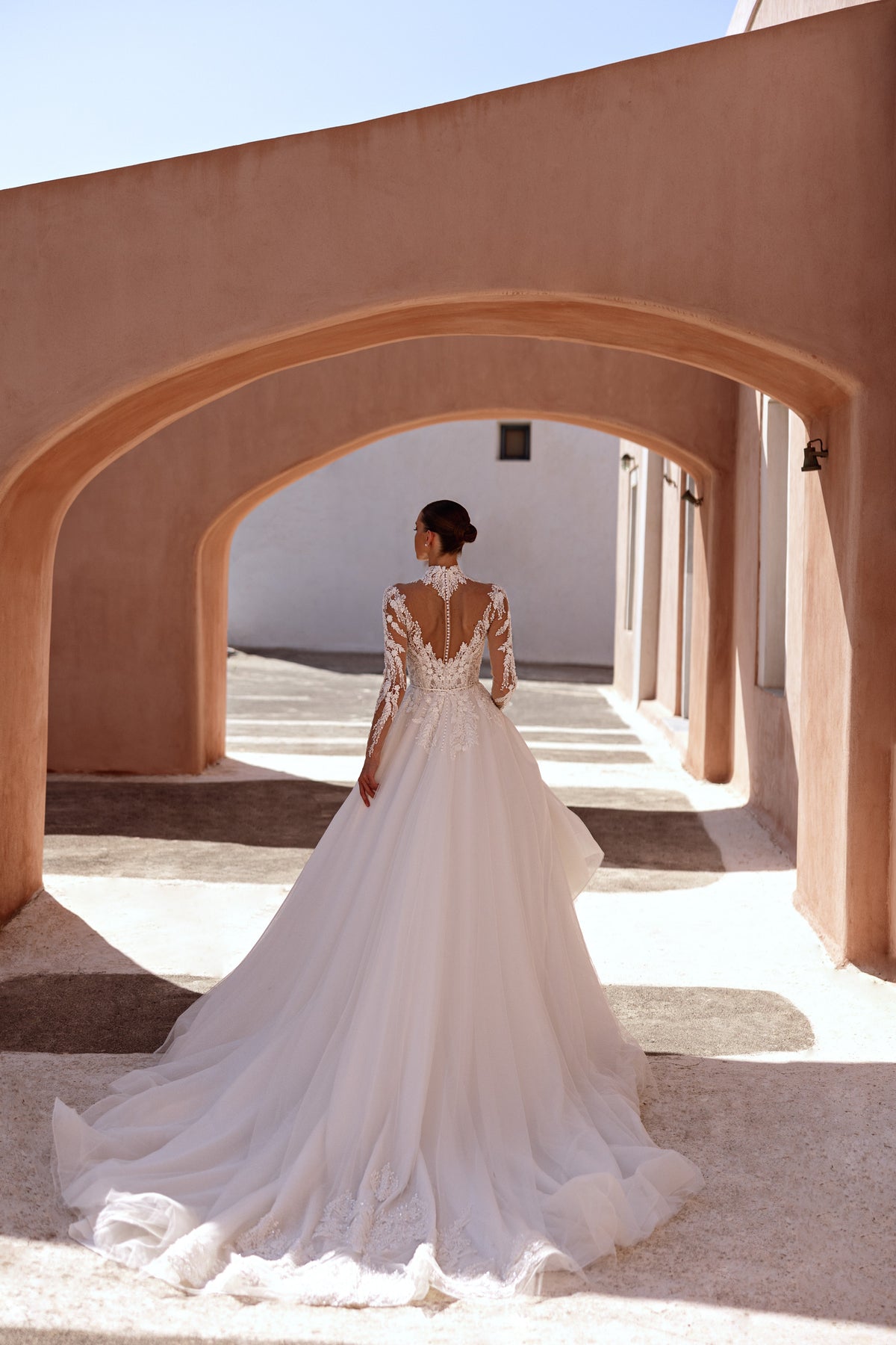 Back of an ivory wedding dress with a sheer lace V-back, covered buttons, and a long train