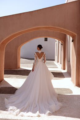 Back of an ivory wedding dress with a sheer lace V-back, covered buttons, and a long train