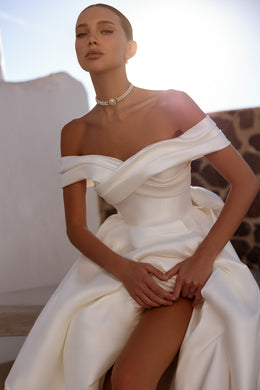 Ivory wedding dress with an off-the-shoulder crossover neckline, fitted bodice, and flowing A-line skirt with a front slit
