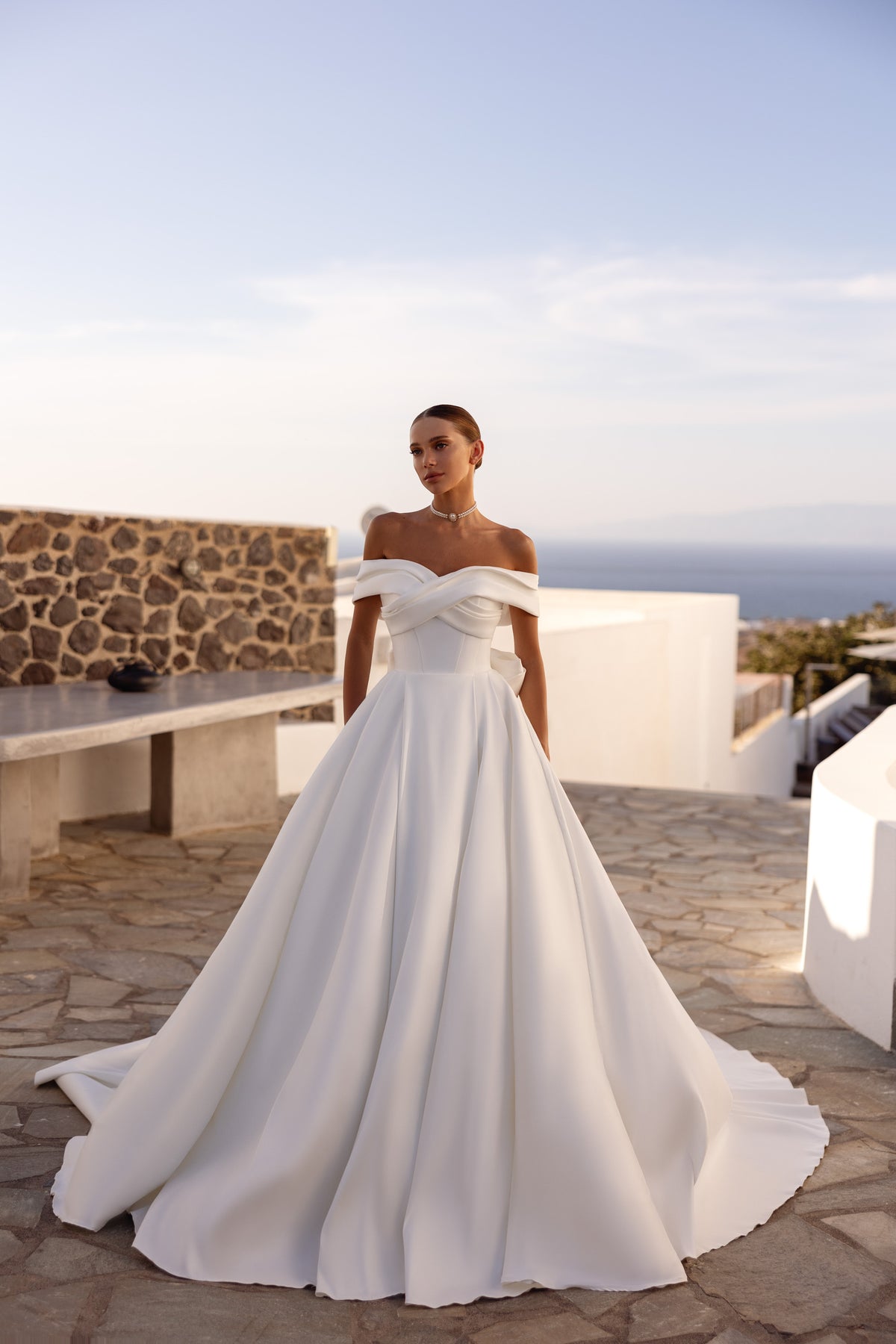 Ivory A-line wedding dress with a sculpted off-the-shoulder crossover neckline and full, floor-length skirt