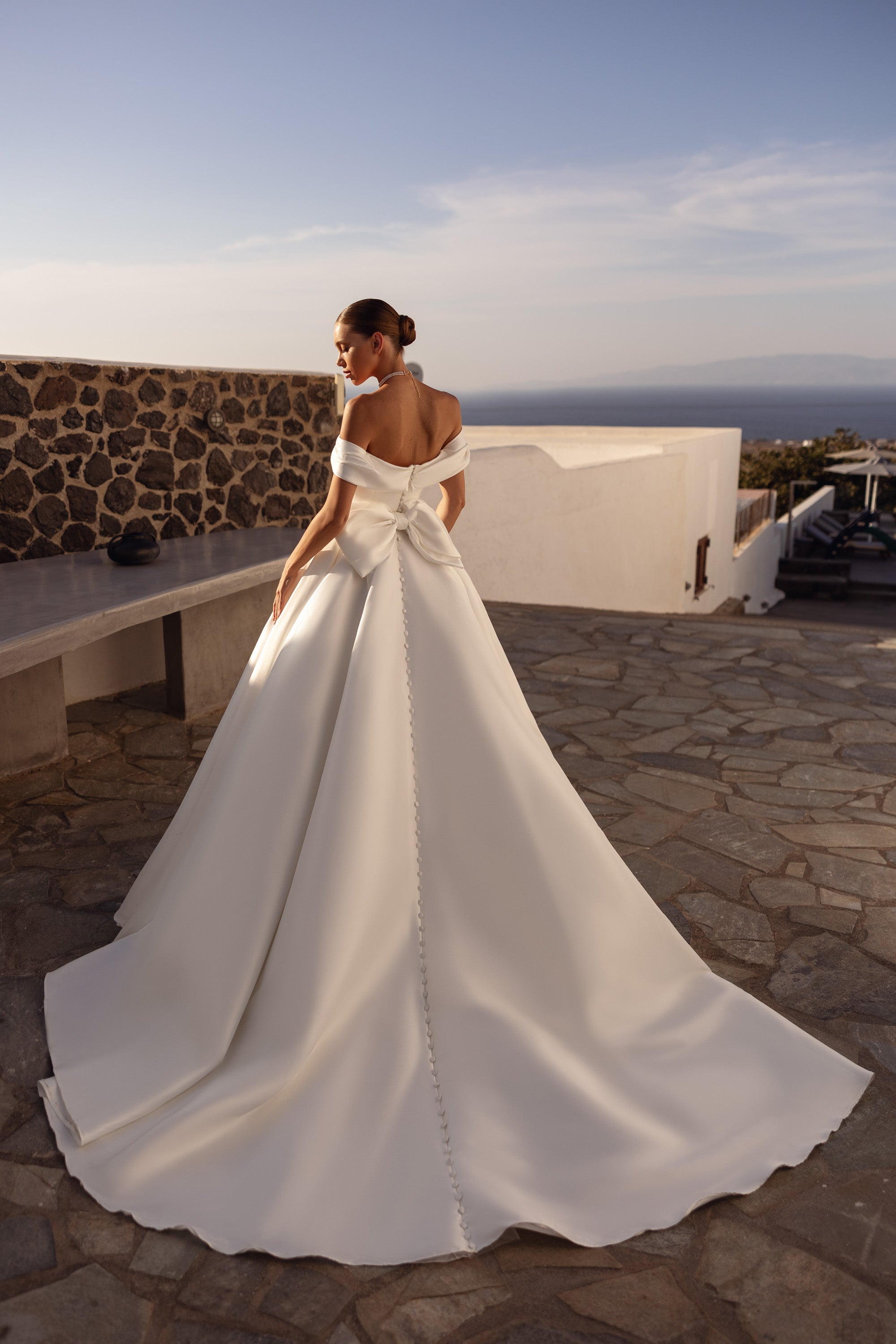 Back view of an ivory wedding dress with an oversized bow, covered button row, and sweeping long train