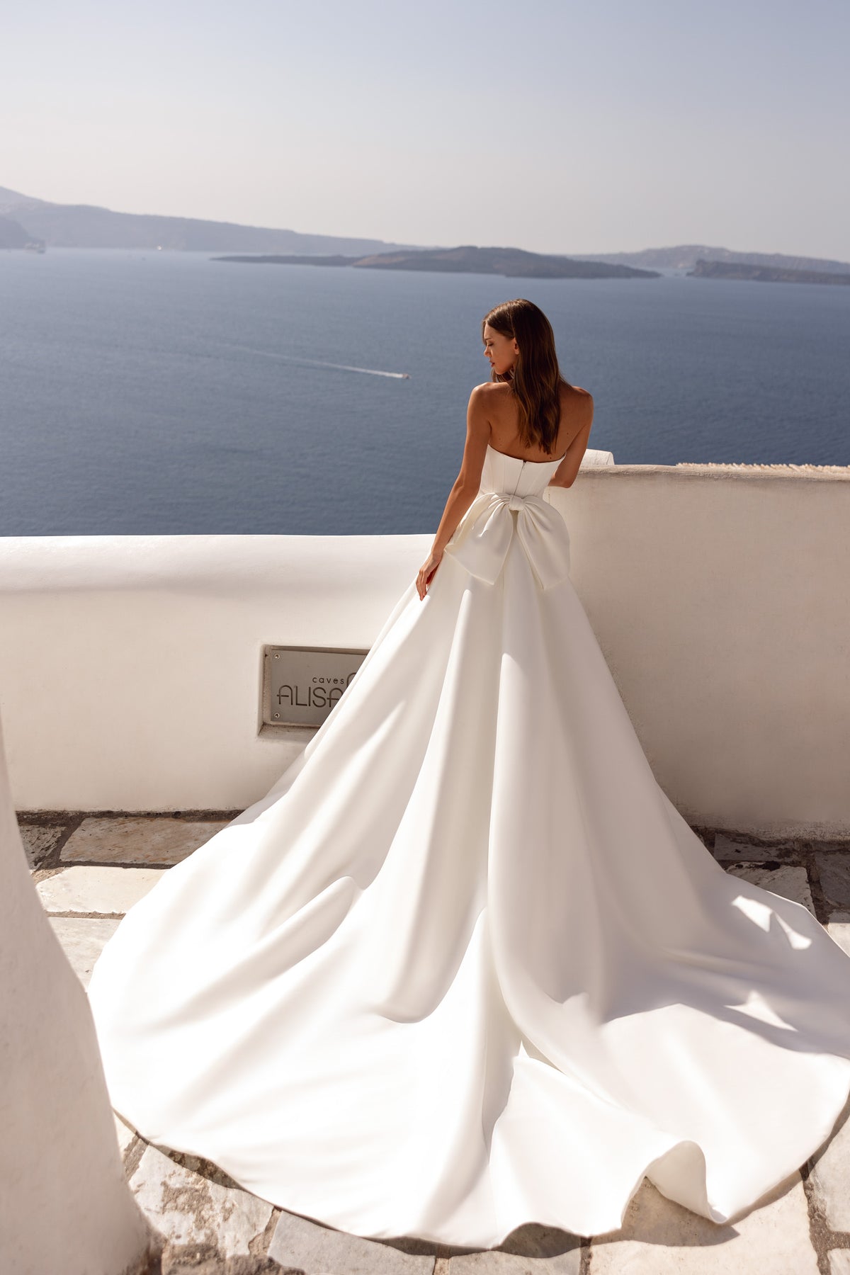 Back view of an ivory wedding dress with a low open back, oversized waist bow, and sweeping floor-length train