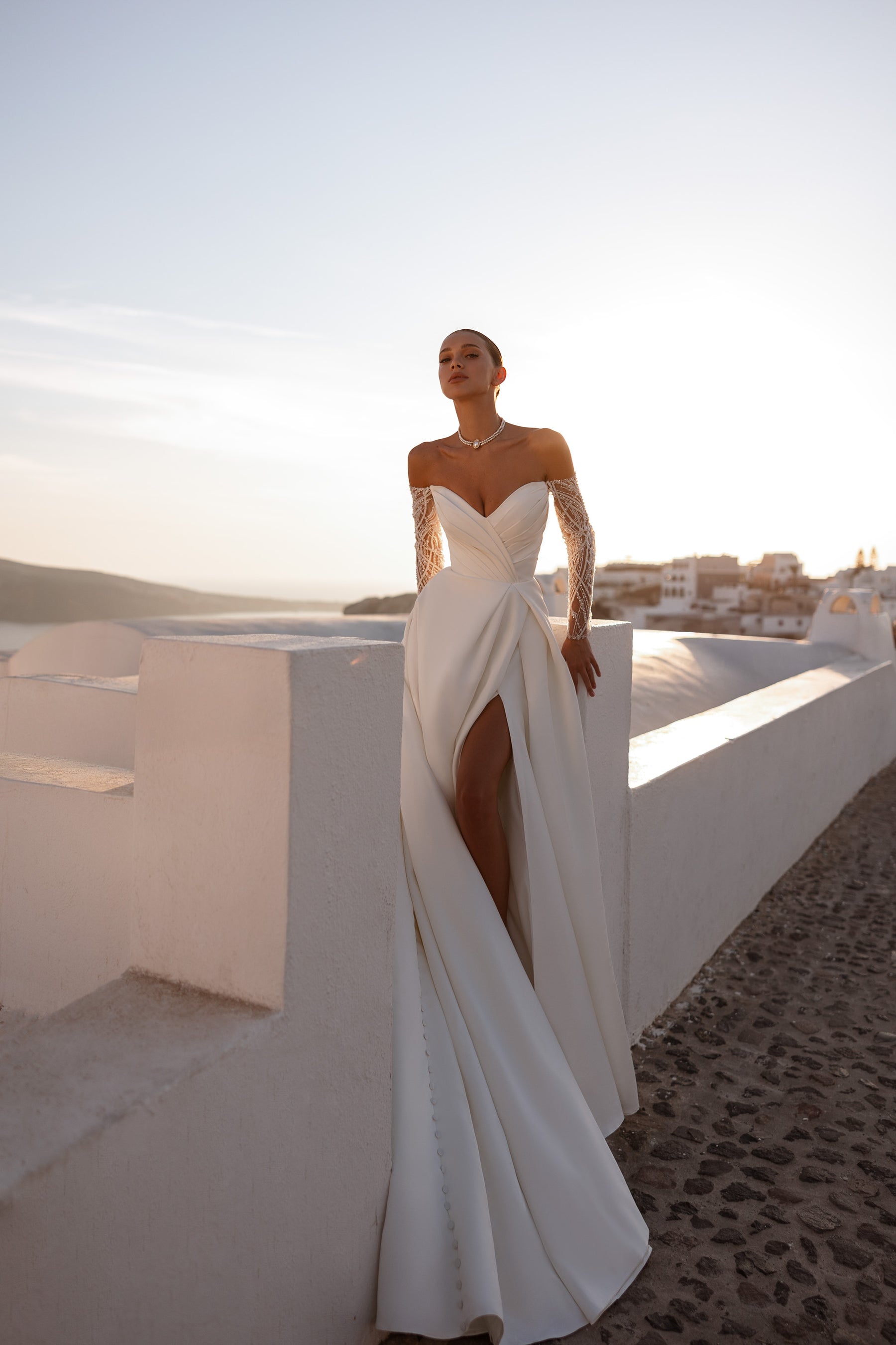 Ivory wedding dress with an off-the-shoulder neckline, sheer lace sleeves, thigh-high slit, and sweeping train