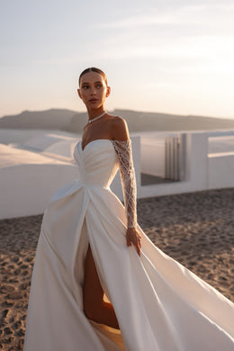 Draped ivory wedding dress featuring long sheer lace sleeves, a gathered sweetheart bodice, and a high slit