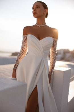 Close-up of the ruched sweetheart bodice, sheer lace sleeves, and thigh slit on an ivory wedding dress