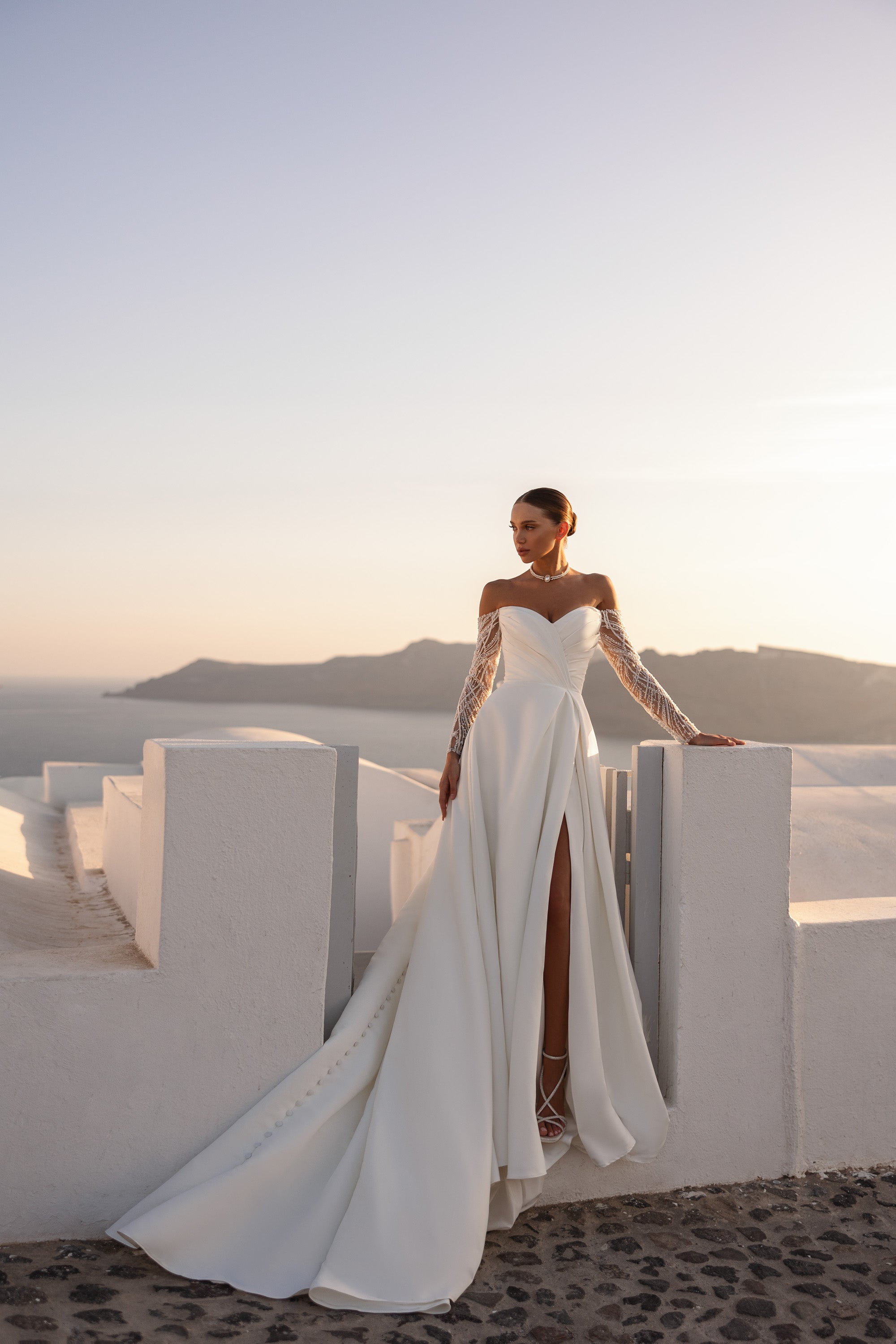 Ivory wedding dress with a long flowing train, off-the-shoulder lace sleeves, and a dramatic front slit